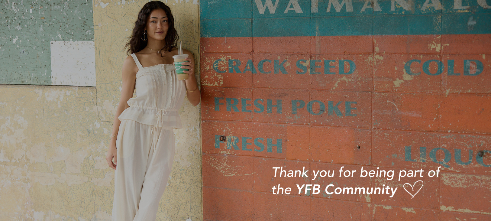 Woman wearing a matching cream tank and harem pant set holding an iced coffee and leaning against a colorful wall.  Text overlay says "Thank you for being a part of the YFB Community"